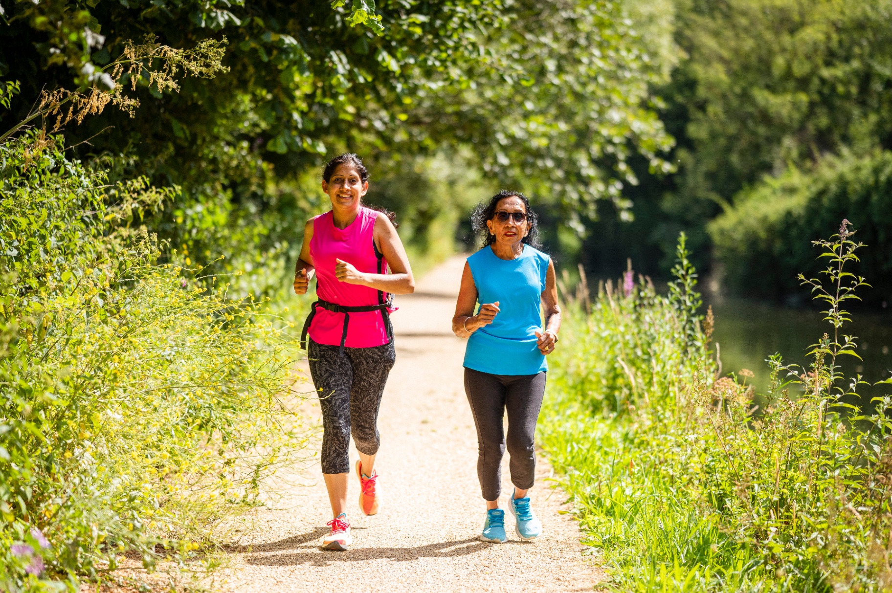 Two women jogging together along a leafy path.