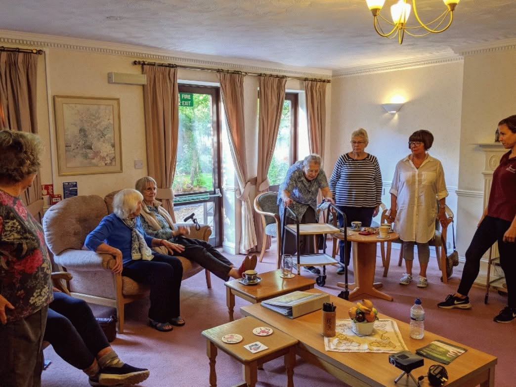 Care home residents in a comfortable lounge taking part in a group session led by a Severn Physiotherapy team member.