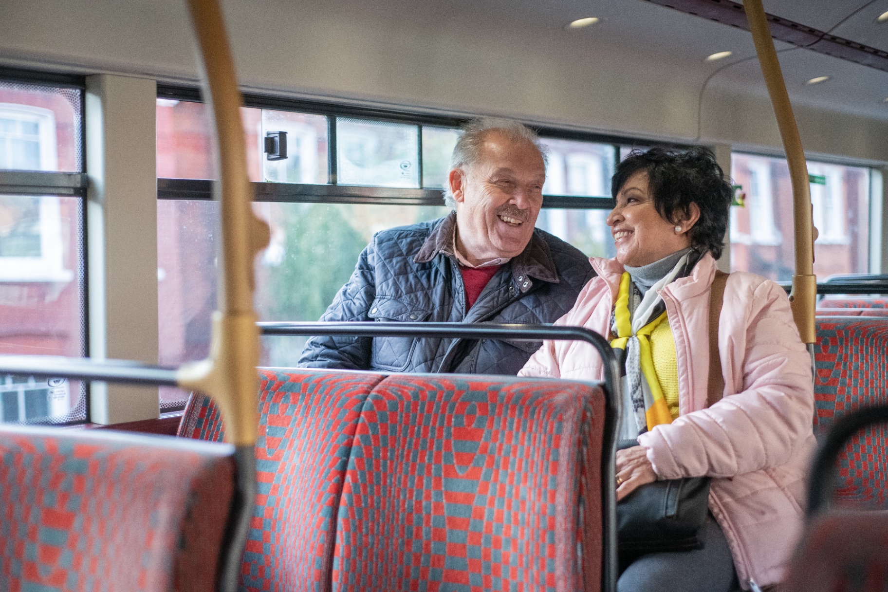 Two older adults smiling together on a bus journey.