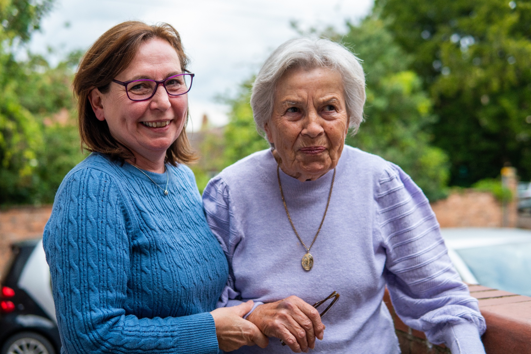A daughter and her elderly mother smiling together outdoors, sharing a warm, connected moment.