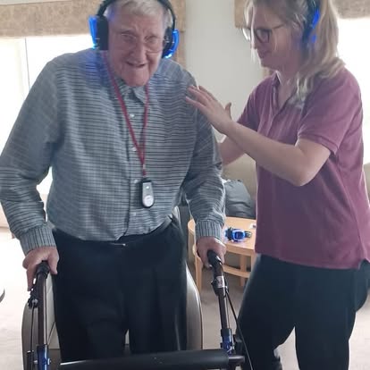 Care home residents wearing wireless headphones, smiling and moving together during a silent disco session.